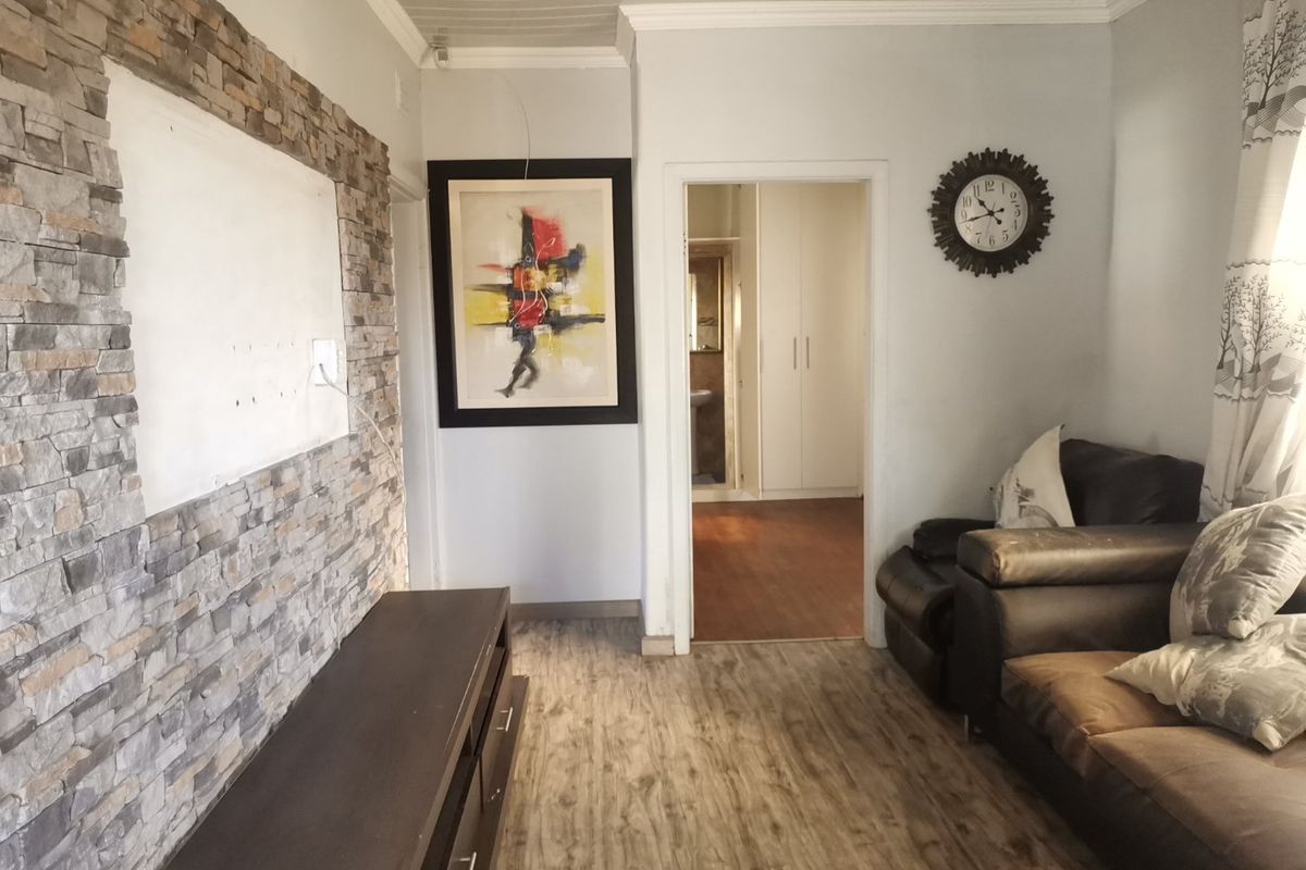 Living room featuring a stone veneer accent wall, laminate flooring, and coved ceilings, with a view through to an adjacent bedroom or hallway.