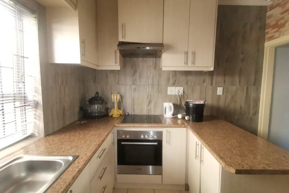Compact kitchen featuring built-in cabinetry, laminate countertops, integrated oven, electric hob, and extractor fan with tiled backsplash and flooring.