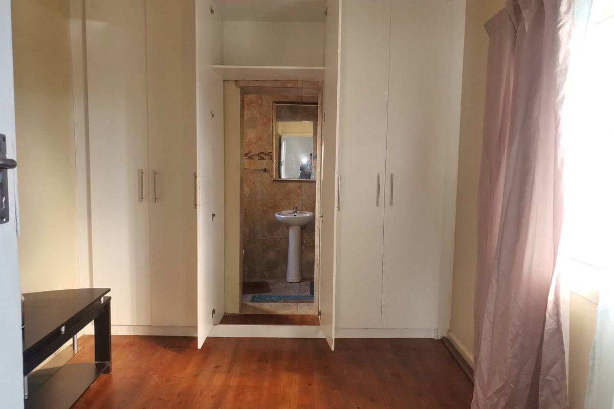 Bedroom featuring built-in cupboards and an en-suite bathroom with a pedestal basin, finished with wooden flooring and neutral wall tones.