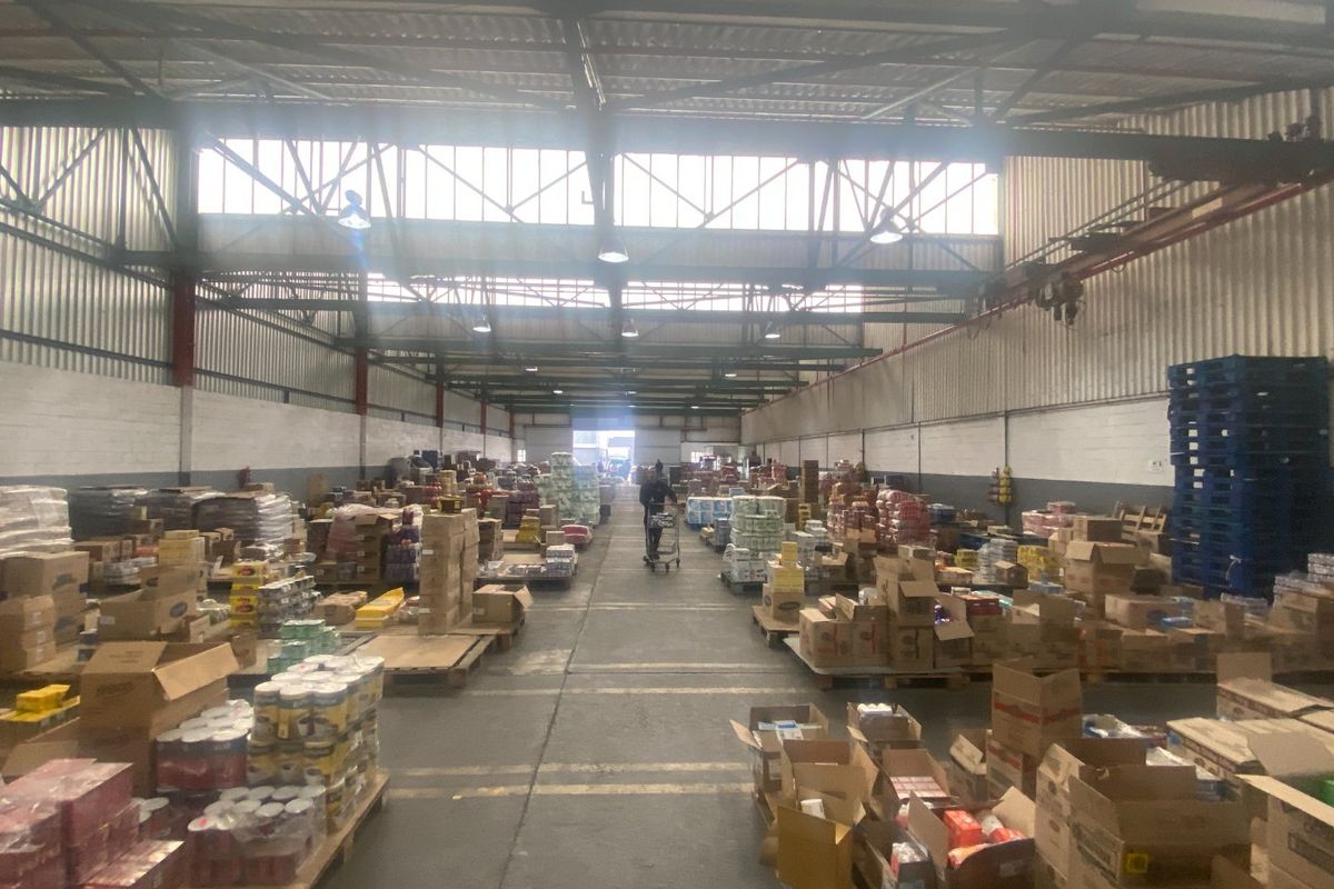 Large industrial warehouse space featuring high ceilings with exposed steel trusses, concrete flooring, and high-bay lighting, currently utilized for storage.