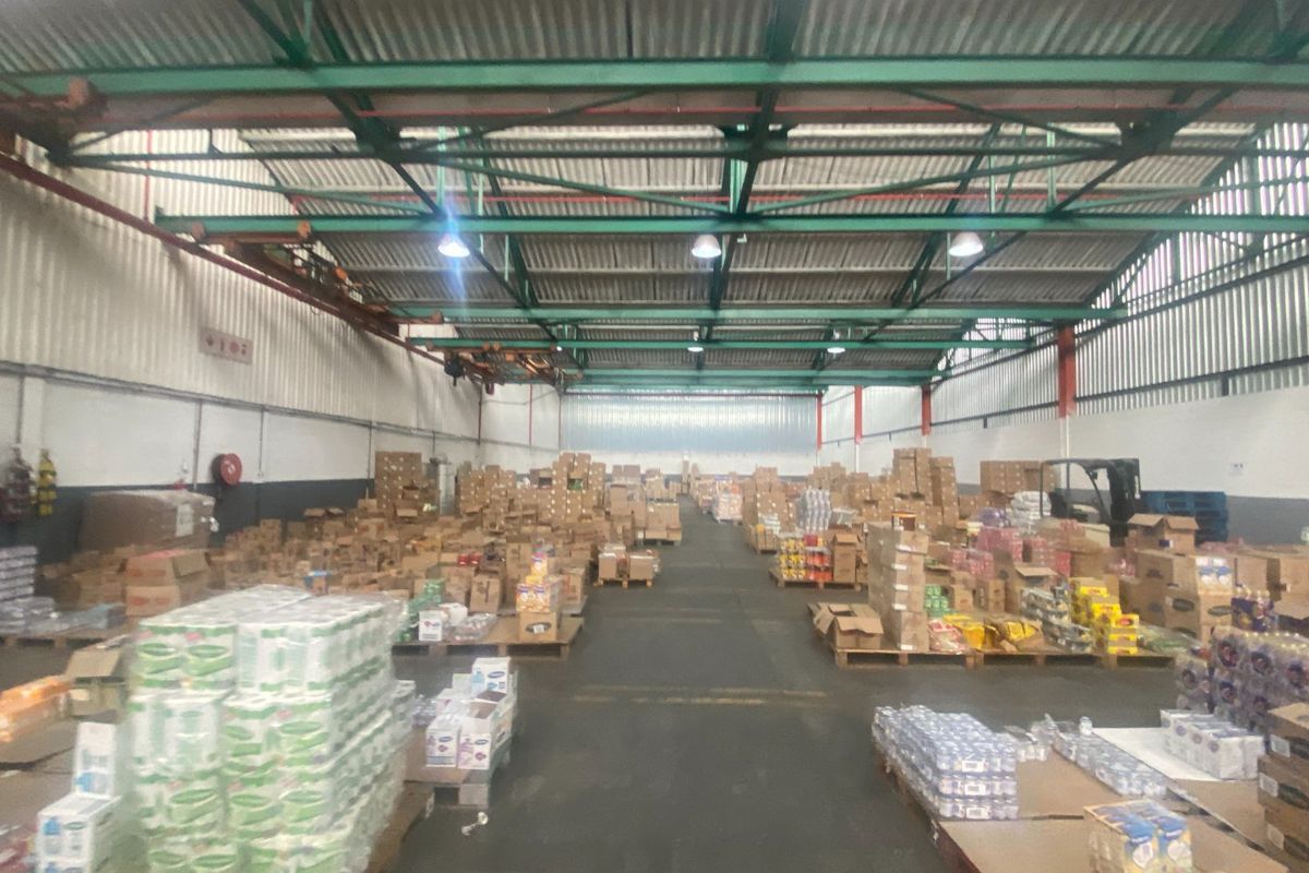 Large industrial warehouse space featuring high ceilings with exposed steel trusses, overhead crane rails, and durable concrete flooring, currently utilized for storage.