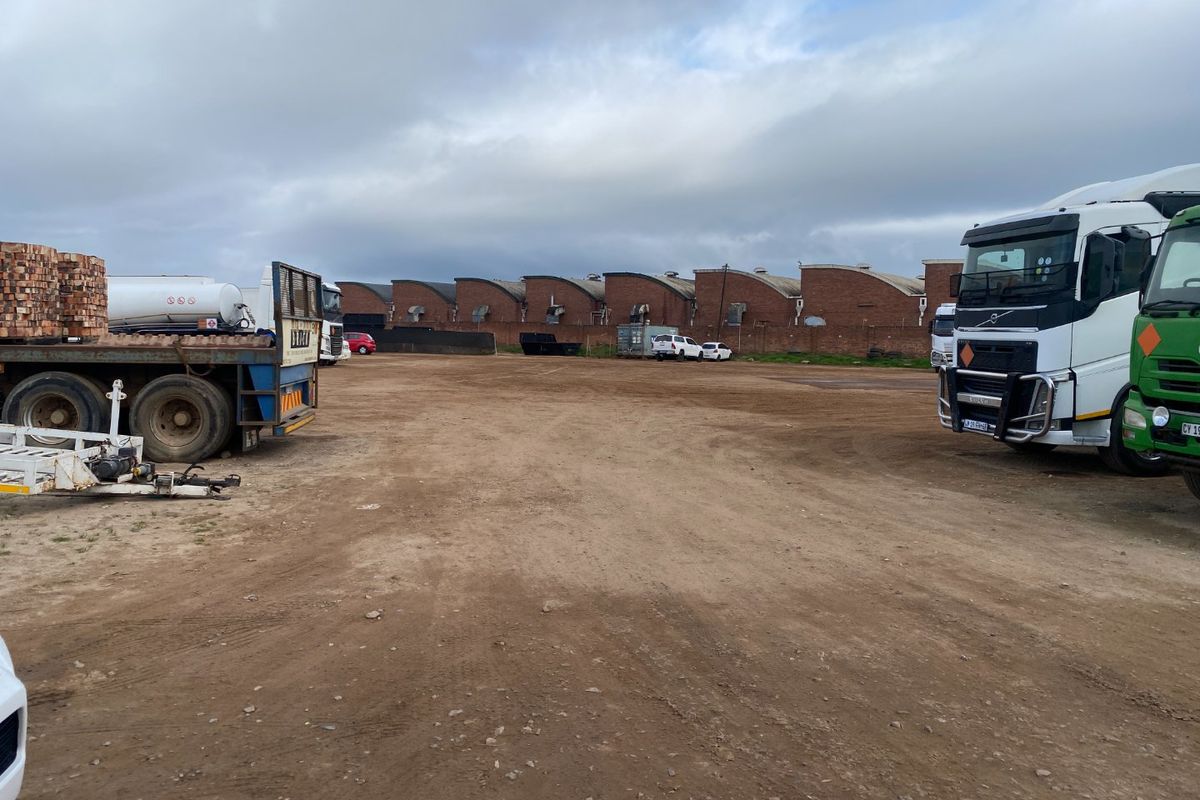 Large industrial yard space featuring a brick perimeter wall and characteristic sawtooth roofline, suitable for heavy vehicle access and storage.