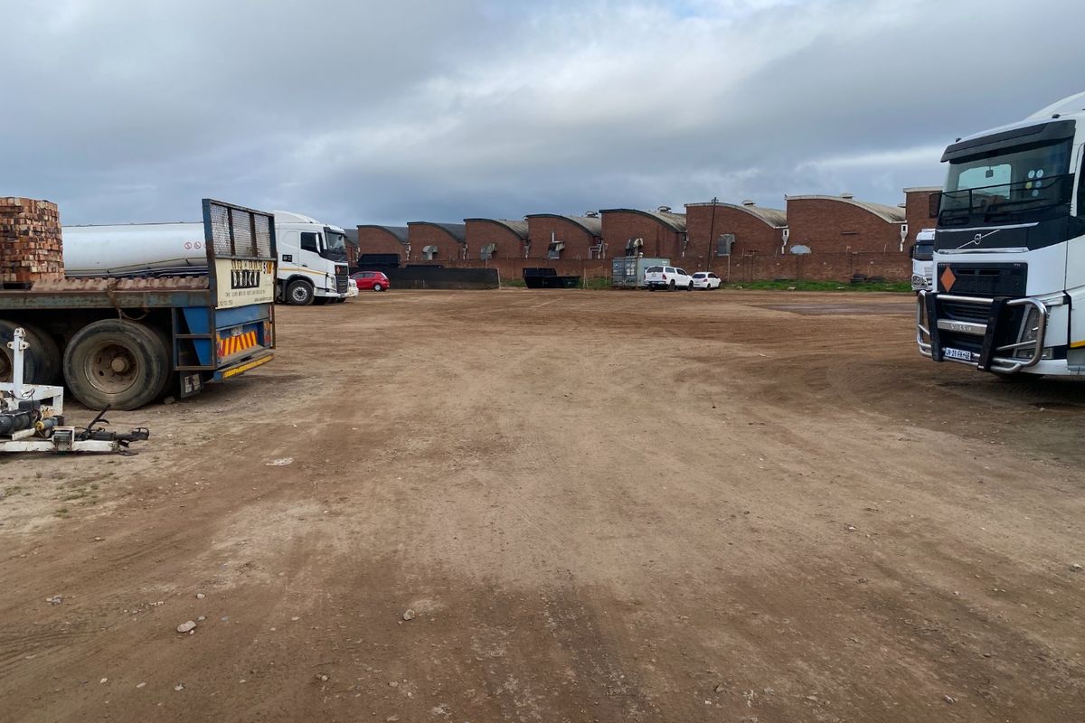 Large industrial yard area featuring an unpaved ground surface and views of the rear warehouse building elevations.