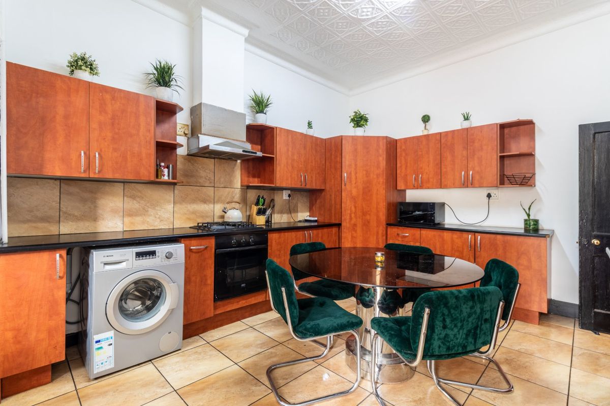A functional kitchen featuring wood-tone cabinetry, dark countertops, a gas hob, integrated oven, and distinctive pressed metal ceiling details.