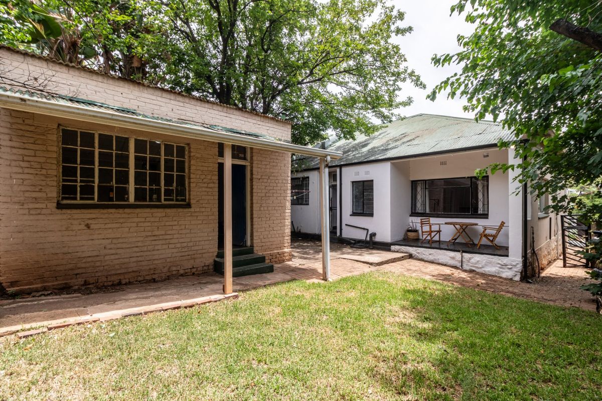 Rear view of the property featuring a brick exterior, covered patio area, and a small garden space with mature trees.