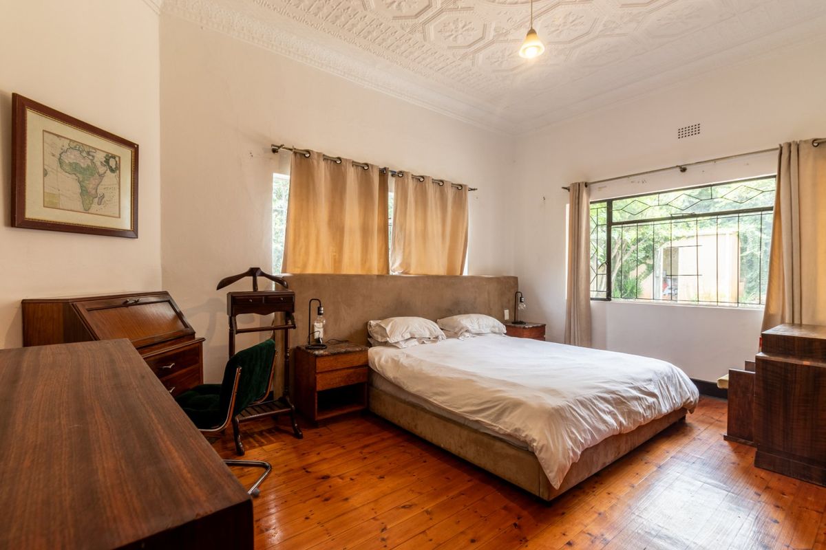 A spacious bedroom featuring original pressed metal ceilings, polished timber flooring, and large windows with security bars, offering a classic architectural aesthetic.