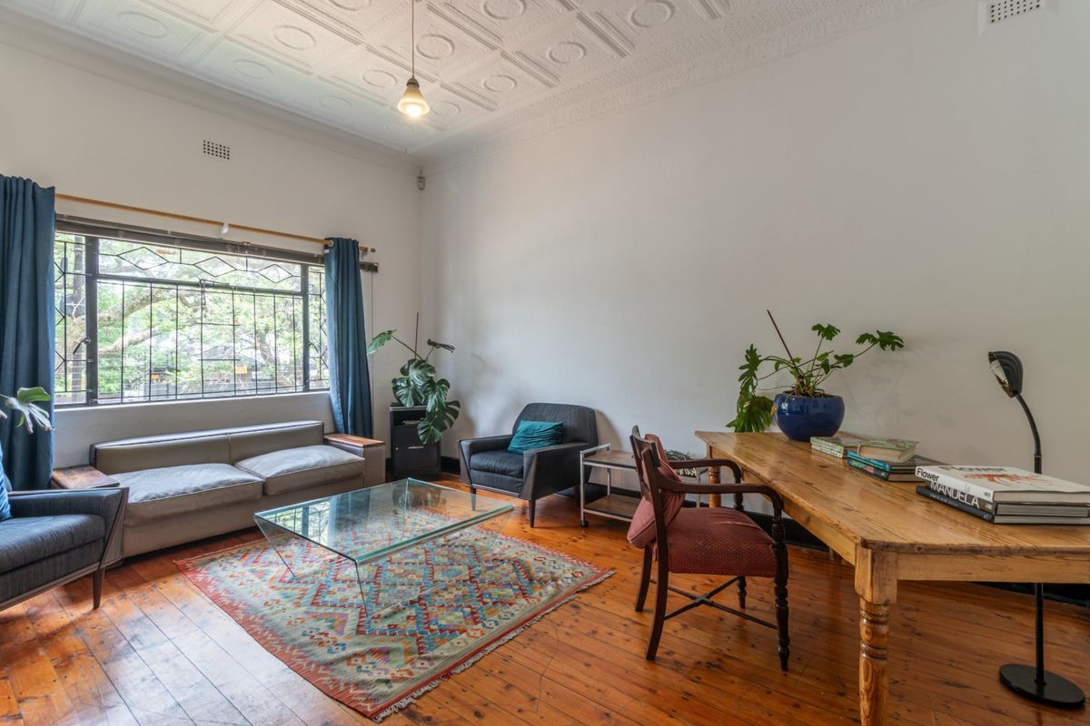 A living room featuring original pressed metal ceilings, polished timber flooring, and a large leaded glass window with security bars.