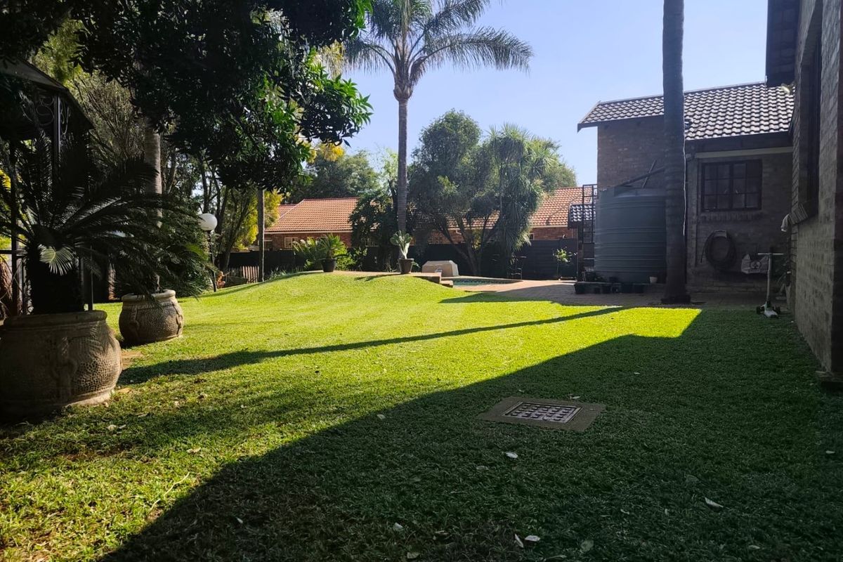 A spacious rear garden featuring a well-maintained lawn, mature trees, a swimming pool, and a water storage tank adjacent to the house.