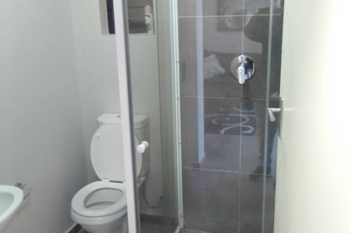 A functional bathroom featuring a glass-enclosed shower, toilet, and wall-mounted basin with neutral tiled finishes.