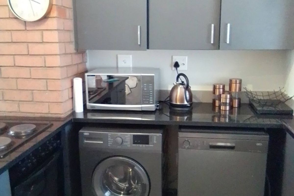 A functional kitchen featuring grey cabinetry, granite countertops, and an exposed brick wall, equipped with a built-in oven and hob.