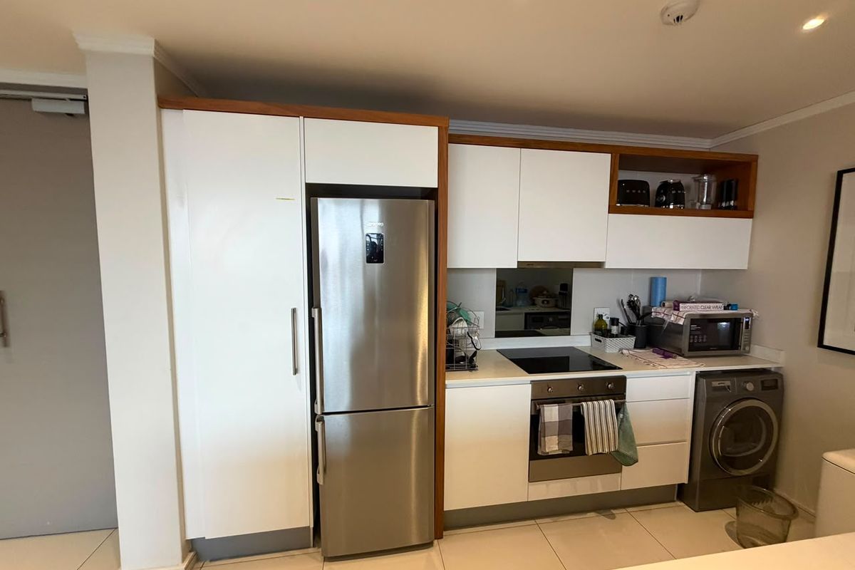Modern kitchen featuring white cabinetry with wood-tone accents, integrated stainless steel appliances, electric hob, oven, and tiled flooring.
