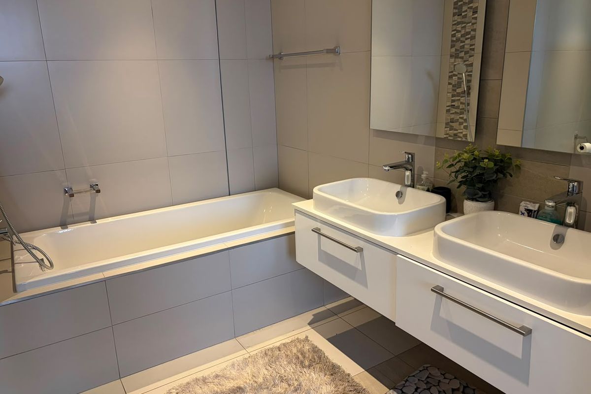 Modern bathroom featuring a built-in bathtub, a wall-mounted double vanity with dual vessel sinks, and neutral floor-to-ceiling tiling.