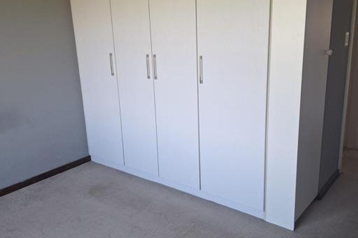 A bedroom featuring neutral walls, carpeted flooring, and a large set of built-in cupboards.
