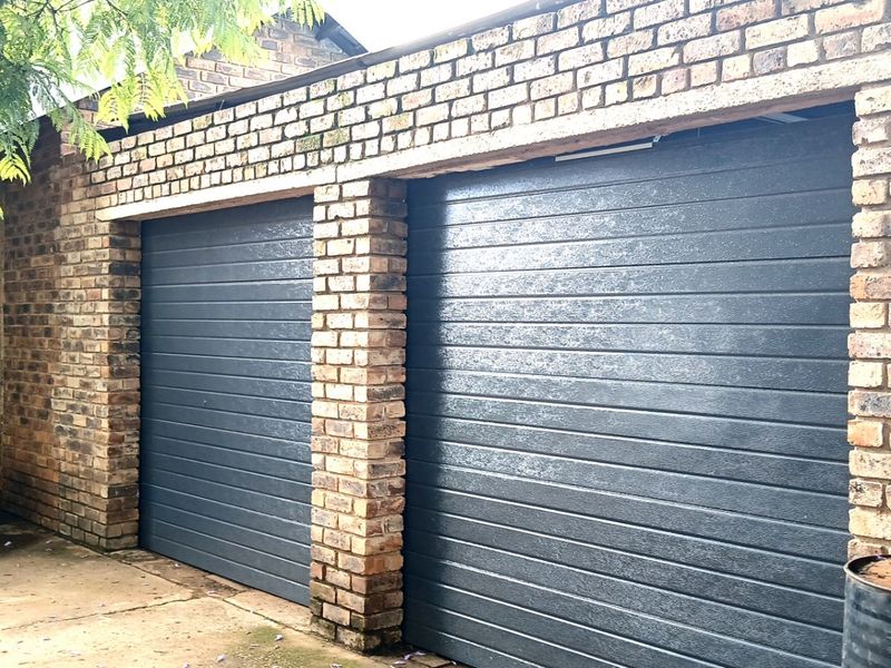 A double garage featuring modern dark grey sectional doors set within a traditional face brick structure.
