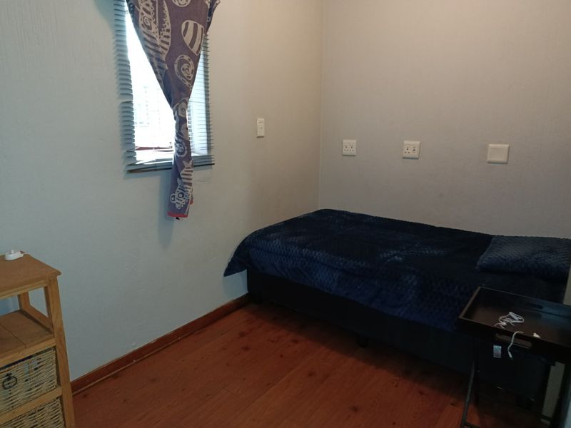 A compact bedroom featuring laminate flooring, a window with venetian blinds, and multiple wall-mounted electrical sockets.