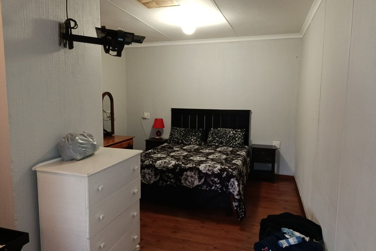A functional bedroom featuring laminate flooring, a ceiling access hatch, and a wall-mounted television bracket, offering a neutral space ready for personalization.