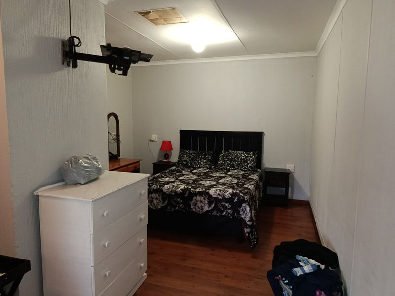 A functional bedroom featuring laminate flooring, a ceiling access hatch, and a wall-mounted television bracket, offering a neutral space ready for personalization.