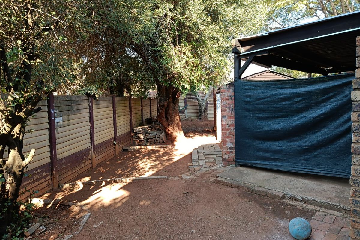 A rear outdoor area featuring a covered patio structure, brick masonry, and a precast concrete boundary wall with mature trees.