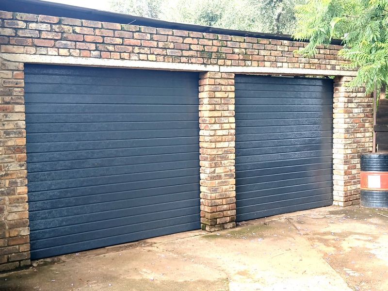 A double garage featuring dark horizontal panel doors set within a face brick structure, complemented by a concrete driveway.