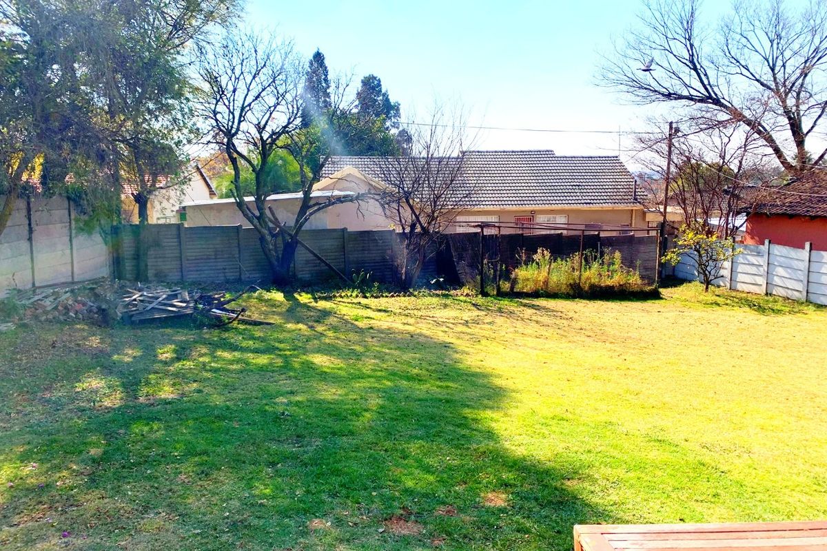 A spacious rear garden featuring a lawn, mature trees, and a precast concrete boundary wall, offering potential for landscaping and outdoor improvement.