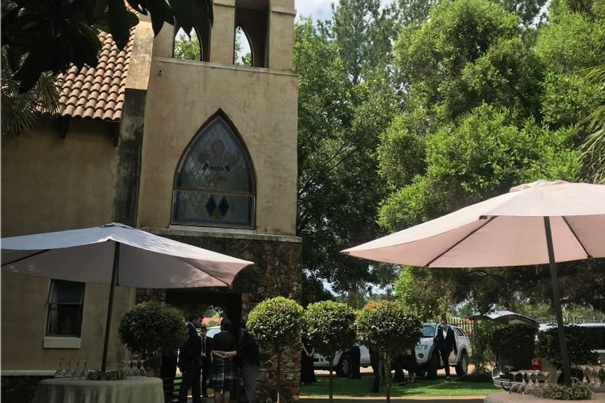 A view of a historic-style building featuring stone masonry, stucco walls, a bell tower, and decorative stained glass windows set within a landscaped garden.