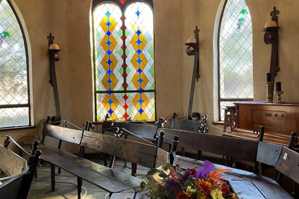 A chapel-style interior space featuring vaulted ceilings with exposed timber beams, ornate stained glass windows, and traditional wrought iron wall sconces.