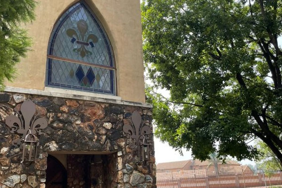 A distinctive commercial building facade featuring stone cladding, a prominent tower, and decorative stained glass windows set within a landscaped garden area.
