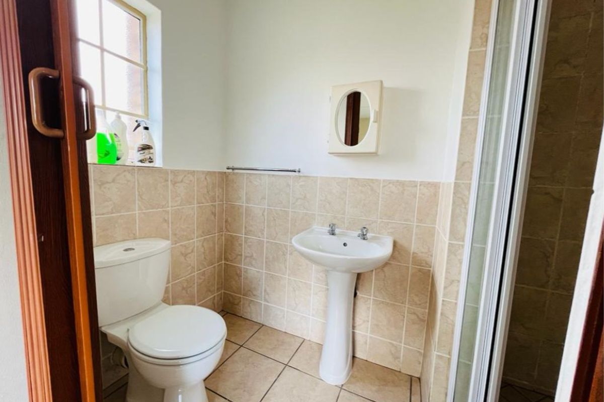A functional bathroom featuring a pedestal basin, toilet, and shower enclosure with neutral wall and floor tiling.