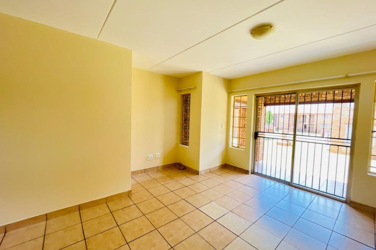 An empty living room featuring ceramic floor tiles, a flush mount ceiling light, and a sliding glass door leading to an outdoor area.