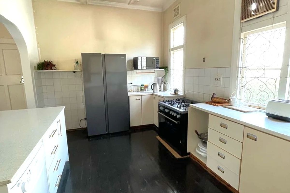 A functional kitchen featuring dark timber flooring, white cabinetry, gas stove, and a distinctive coffered ceiling, offering potential for modern renovation.