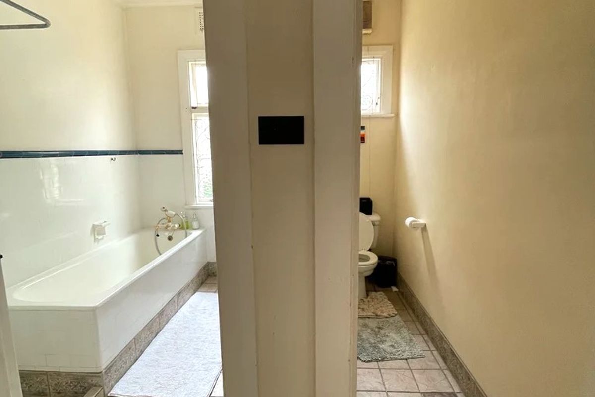 A dated bathroom featuring a separate bathtub area and toilet, with tiled flooring and wall finishes in need of cosmetic updates.