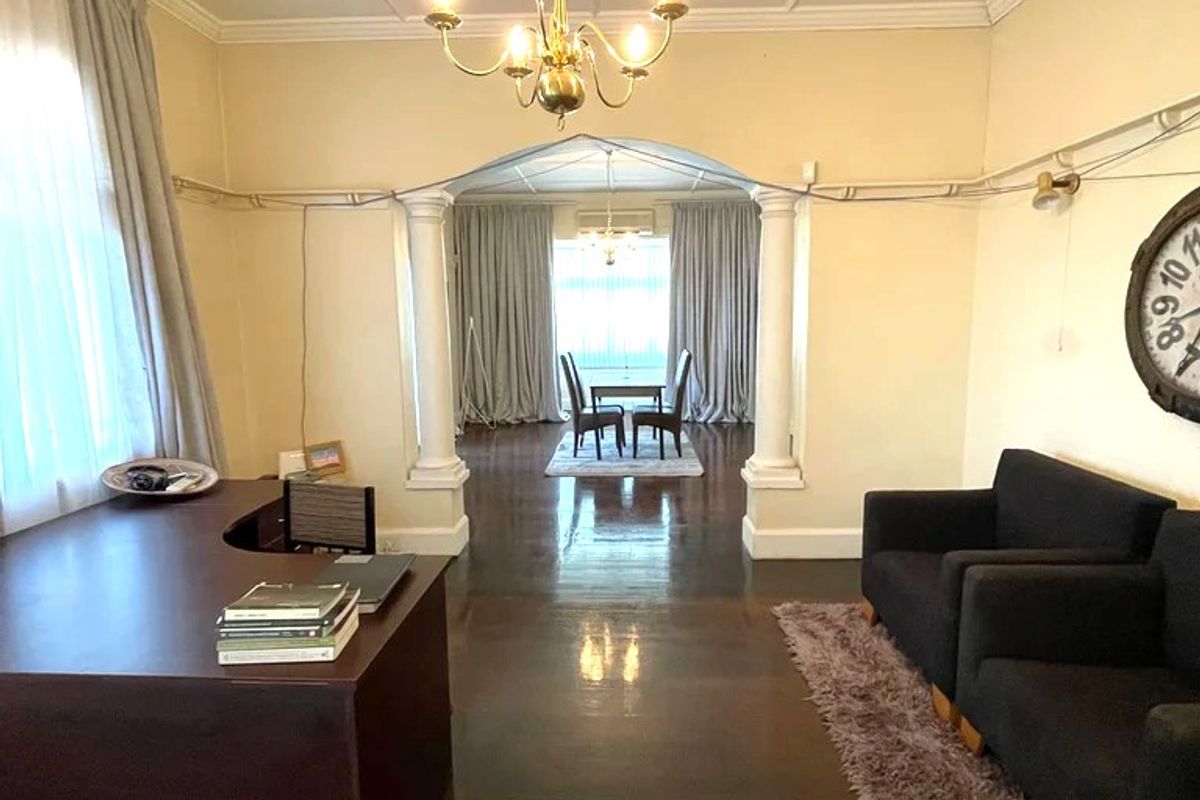 Spacious living area featuring hardwood floors, decorative columns, and a coffered ceiling, leading through an archway to an adjacent dining space.