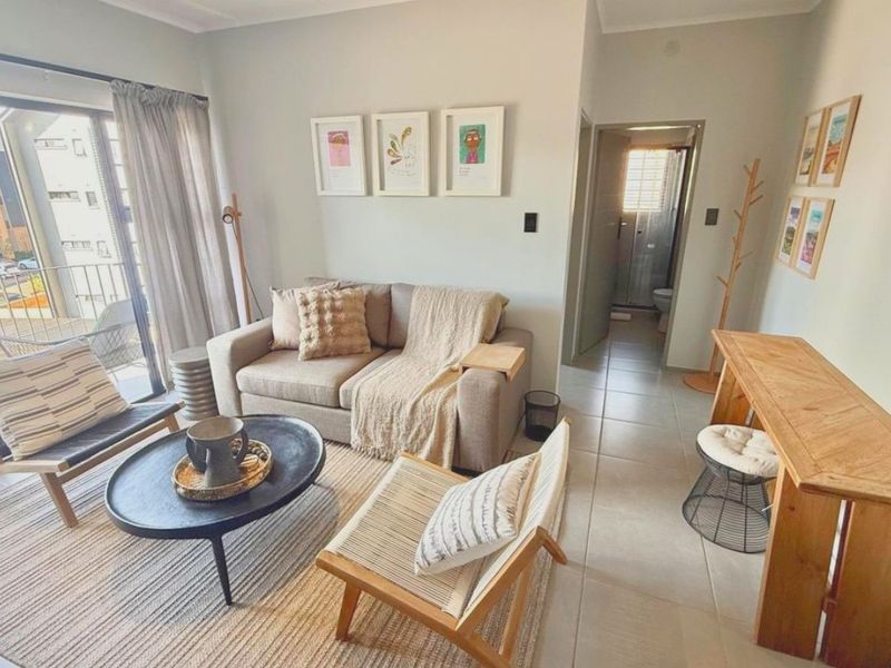 A bright and well-maintained living room featuring neutral tiled flooring and a sliding glass door providing access to an outdoor balcony area.