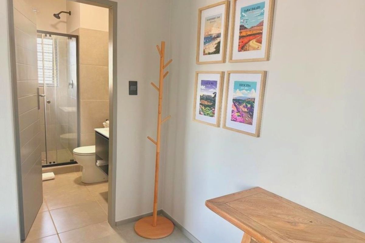 A clean, modern bathroom featuring a glass-enclosed shower, toilet, and vanity cabinet, accessed from a neutral-toned hallway.