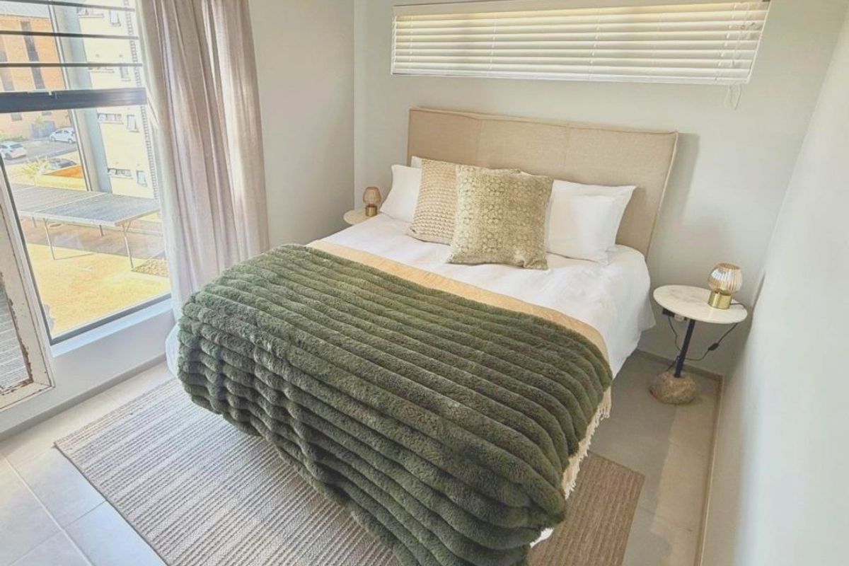 A bright and well-maintained bedroom featuring large windows with venetian blinds and neutral tiled flooring.