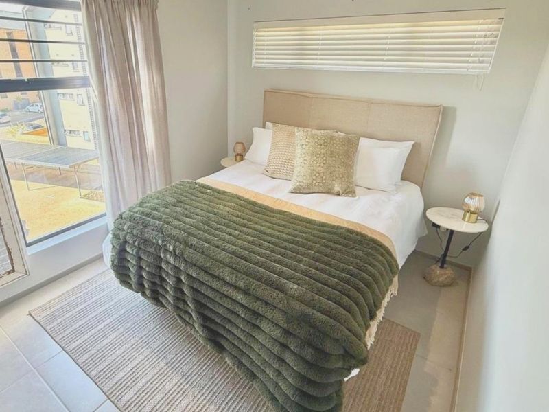 A bright and well-maintained bedroom featuring large windows with venetian blinds and neutral tiled flooring.