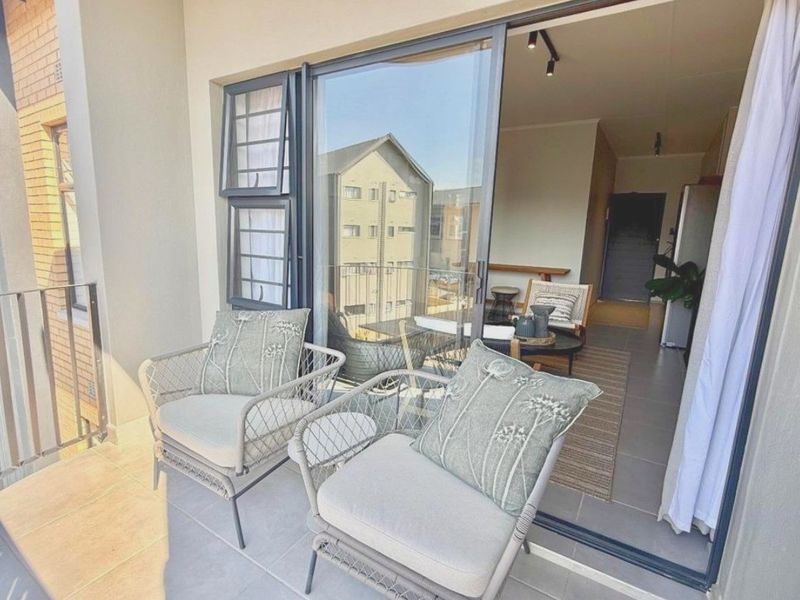 A modern apartment balcony featuring tiled flooring, a metal balustrade, and large sliding glass doors providing seamless access to the interior living space.
