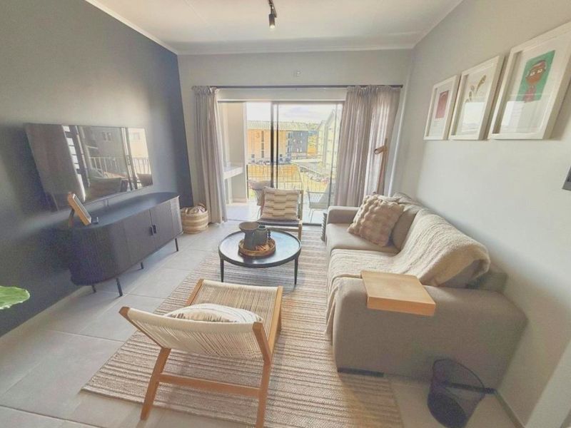 A well-lit living room featuring tiled flooring, a dark accent wall, and a sliding glass door providing access to an outdoor balcony area.