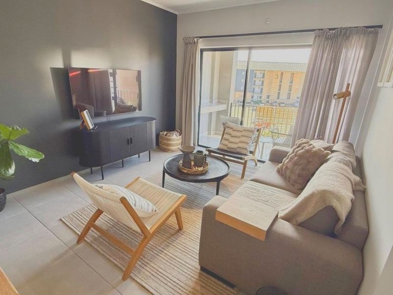 A well-lit living room featuring an accent wall, tiled flooring, and a large sliding glass door providing access to an outdoor balcony area.
