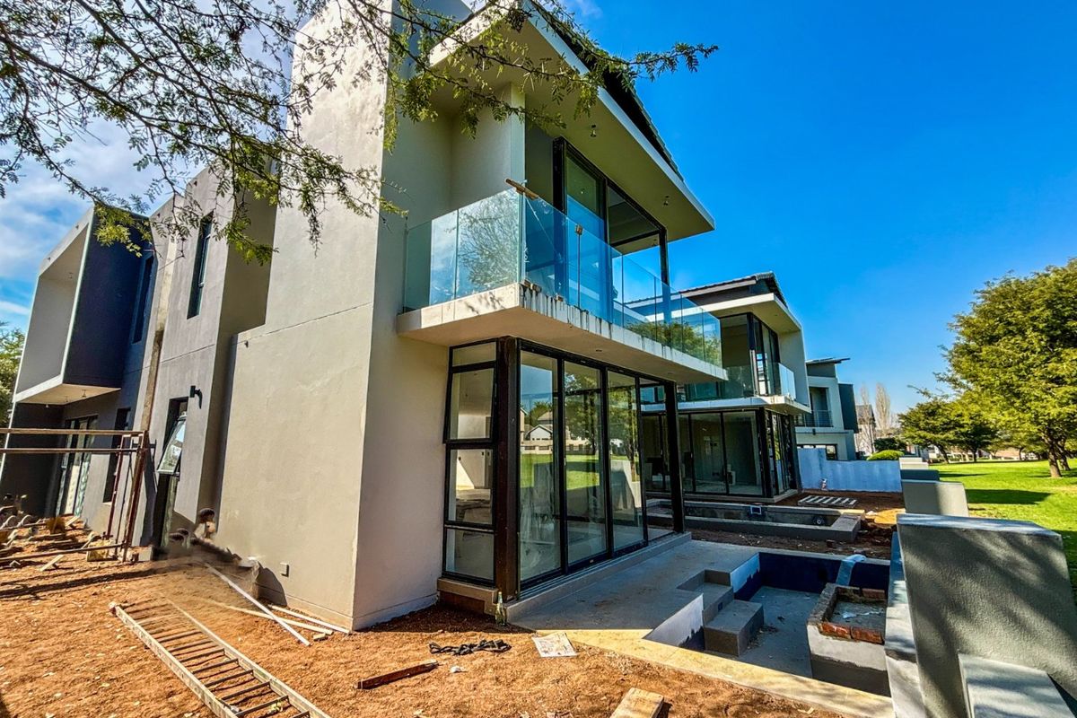 Rear view of a modern multi-story residence featuring glass balconies, large sliding doors, and an unfinished swimming pool area under construction.