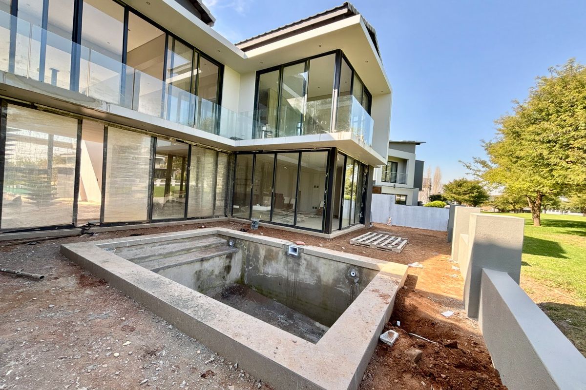Rear view of a modern two-story house under construction, featuring large glass sliding doors, glass balustrades, and an unfinished swimming pool in the backyard.