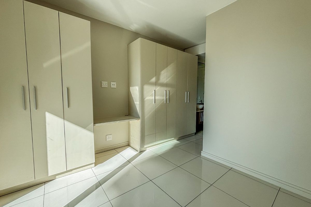 A bright, empty bedroom featuring extensive built-in cupboards, a integrated desk area, and clean tiled flooring throughout.
