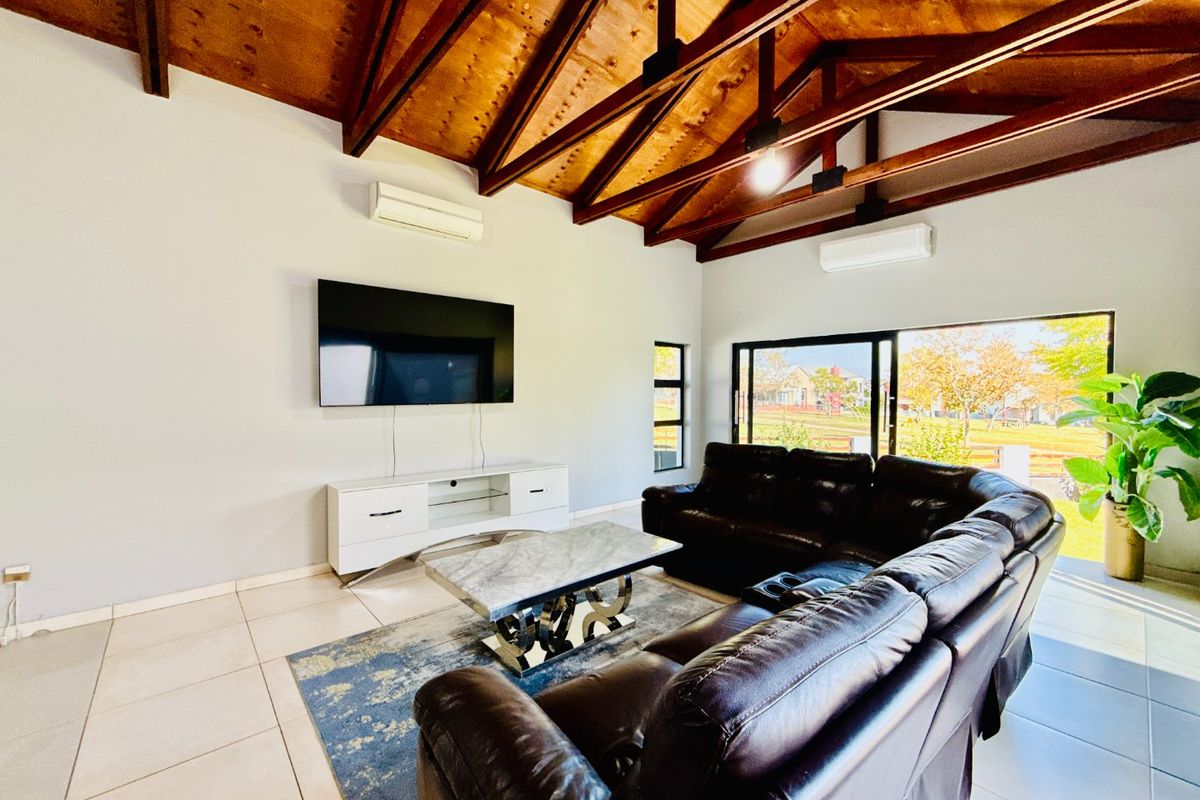 Spacious living room featuring a high vaulted ceiling with exposed timber rafters, tiled flooring, dual air conditioning units, and large sliding doors to the garden.