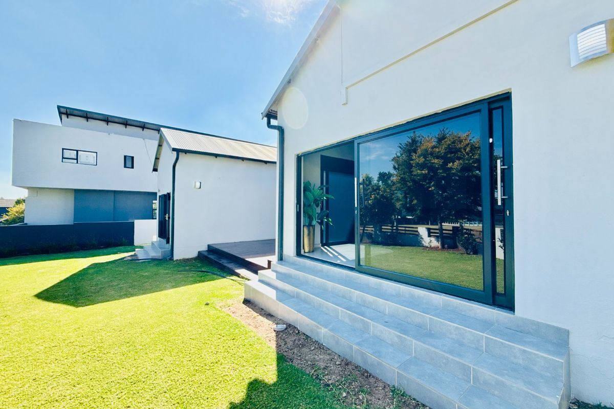 Rear exterior view featuring a modern home with large sliding glass doors, tiled patio steps, and timber decking leading to a well-maintained lawn.