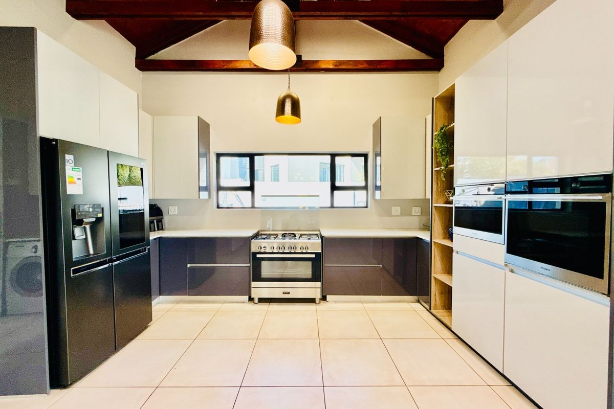 Modern kitchen featuring high-gloss cabinetry, a gas stove, built-in ovens, and striking exposed timber ceiling beams with contemporary pendant lighting.
