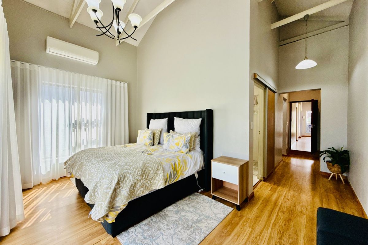 Spacious bedroom featuring high vaulted ceilings with exposed rafters, laminate flooring, and an integrated split-system air conditioner, leading to an en-suite bathroom.