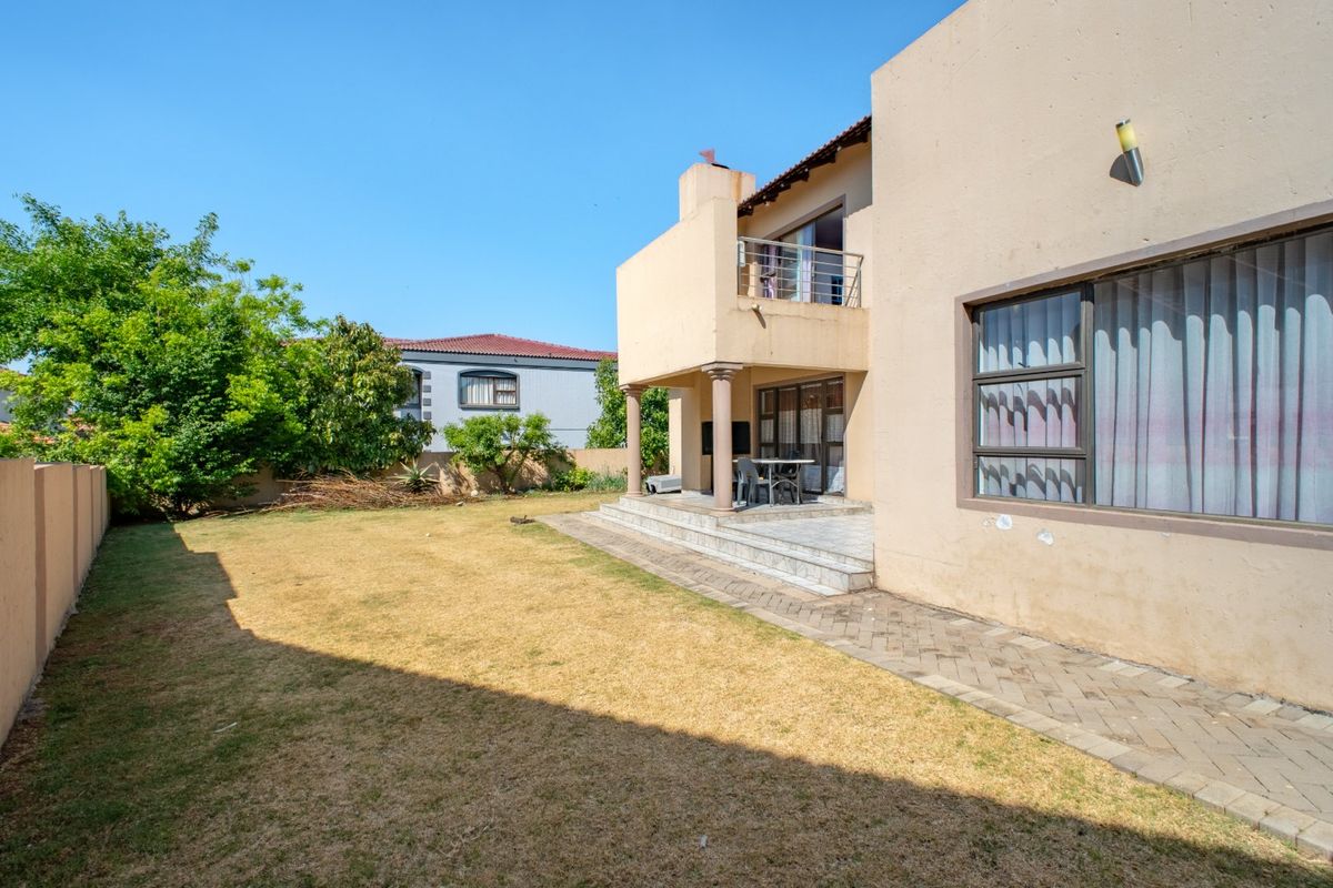Rear view of the property featuring a covered patio, an upper-level balcony, paved walkways, and a private garden area with boundary walls.
