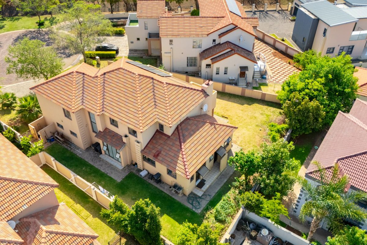 Aerial view of a residential property featuring a terracotta tiled roof, solar panels, and a well-maintained garden within a secure estate setting.