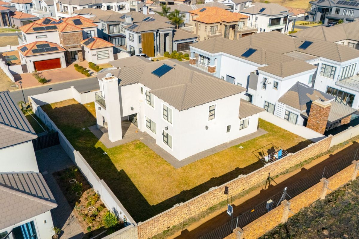 Aerial view of a modern double-story residential property featuring a tiled roof, solar panels, and a private garden enclosed by a perimeter wall.