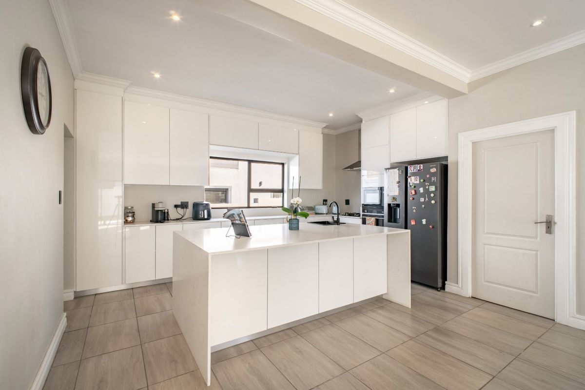 Modern kitchen featuring a central island with quartz countertops, sleek white cabinetry, built-in appliances, and neutral tiled flooring.